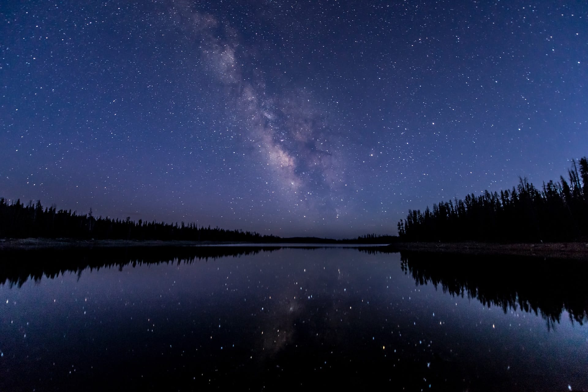 A breathtaking view of the starry night sky and the Milky Way galaxy over a serene, lost lake in the Uinta Mountains. The celestial display above the tranquil waters creates a majestic and awe-inspiring scene, symbolizing the vast and unexplored depths of the subconscious mind and the journey of self-discovery.