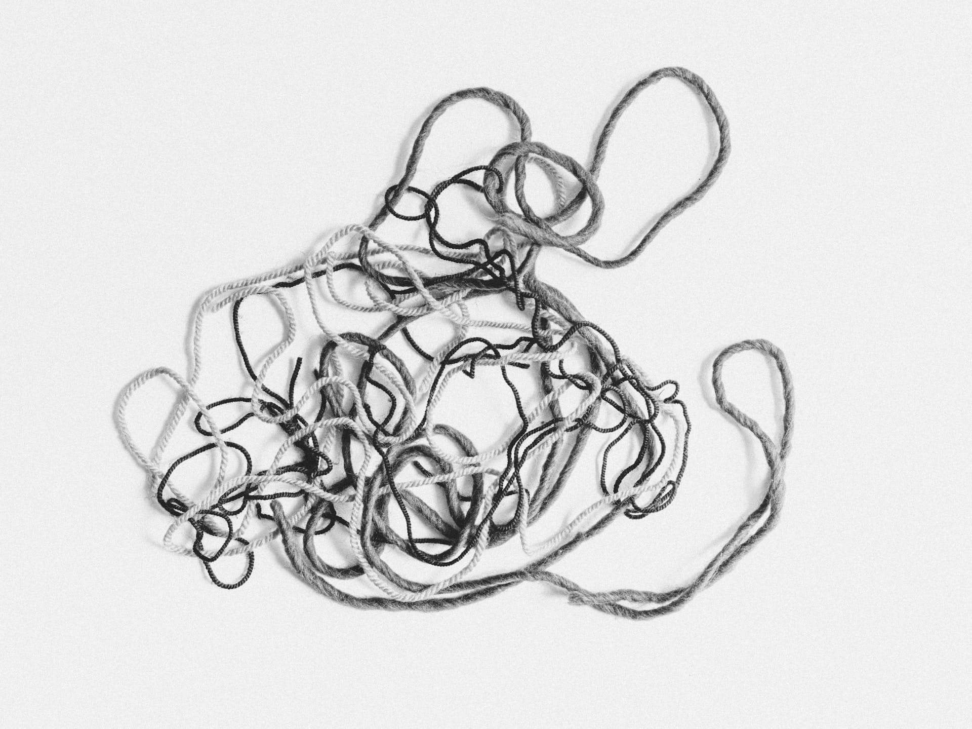 A grayscale image of tangled yarn, symbolizing the complex and intertwined nature of thoughts within the subconscious mind. The monochromatic tones highlight the yarn's intricate patterns and knots, visually representing the journey of unraveling and understanding one's inner thoughts and feelings through introspection.
